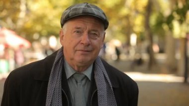 Düz bir kapak, neşeli komuta sizde kravat ve ayakta ceket ve ekose düz bir kapak iş bir zarif yaşlı adamın bir park Bokeh portre bekleyen takım elbise, kravat ve gülümseyen ve gösterişli bir parkta sonbaharda bekleyen uzun ceket
