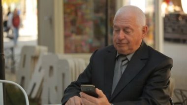 Bir kafede otururken ve akıllı bir komuta sizde bir kafede otururken, net tarama ve bir sokakta biraz bilgi arayan bir takım elbise içinde muhteşem manzarası sonbaharda telefonundan net sörf akıllı ihtiyar 