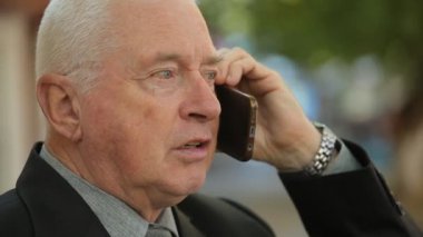 Güz profil güvenilir üst düzey işadamı derli toplu bir takım elbise ve bir yeşil sonbaharda sokak kavmine onun smartphone üzerinde talimat verirken bir kravat çalışanlarına bir sokakta ile telefonda konuşurken ciddi yaşlı adam