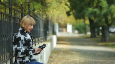 Çabuk anne ve parapetin üzerinde oturan ve seyir ile bir telefon ve onun genç adam onu yaklaşıyor ve bir parkta parapetin bir koltuğa alarak Güz etkileyici profil Ekose ceketli sarışın bir kadının telefon cesur oğlu