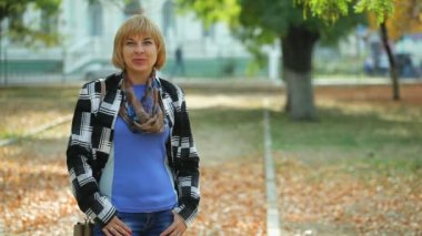 Ayakta ve neşeli yeşil bir sonbahar heyecanlı bokeh portre güzel bir sarışın kadının sokakta bir trendy ceket daimi yeşil bir parkta sonbaharda güneşli bir günde bir bob saç kesimi ile gülümseyen şık sarışın kadın