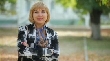 Ayakta ve memnuniyetle bir parkta yeşil zarif bir sarışın kadının sonbahar duygusal bokeh portre güneşli bir sonbahar içinde yeşil bir arka sokakta bir moda ceket daimi bir bob saç kesimi ile gülümseyen glamour sarışın kadın