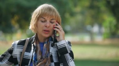 Yeşil bir parkta telefonunda bir dinamik sarışın kadının ekose bir yün ceket ve onun Smartphone'da sohbet ve gülümseyen bir eşarp sonbahar Bokeh portre sonbaharda bir arka sokakta neşeli etkin sarışın kadın söz.