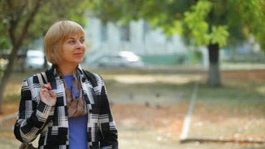Gülümseyen oğlu ile bir parkta brunet oğlu için bekleyen siyah ve beyaz Ekose ceketli gülümseyen bir sarışın anne harika manzarasını sarı trefoil için bekleyen mutlu sarışın kadın onu sarılma ve veren sonbahar yaprakları