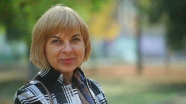 Mutlu bir şekilde sonbaharda sarı bir parkta gülümseyen zarif bir ekose ceket giymiş esrarengiz gözlerle sonbahar harika bokeh görünümü şık bir sarışın kadının yeşil bir parkta duran parlak gözlü akıllı sarışın kadın