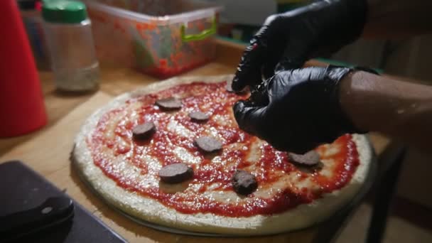 ピザを作ると エキサイティングなスローモーションで生地にサラミを拡散の手袋で男の手が黒手袋イタリアのピザを作ると スローモーションでトマト パスタと生地をフラットでサラミの輪切りを設定で男性の手の表示します — ストック動画