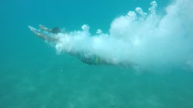 Genç adam baş aşağı kabarcık ile deniz sularında ağır çekimde kabarcıklar onu ağır çekimde çevreleyen bir sürü ile çarpıcı çekim bir genç adam dalış kafa şeffaf mavi deniz sularında ilk patlama taşır. Daha sonra ileri yüzüyor.