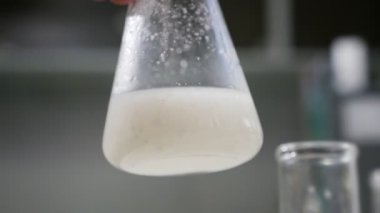 Süt ile üçgen şişesi ağır çekim heyecanlı portre yavaş yavaş kalite kontrol etmek ve slo-mo süt çözümleme yapmak üzere taşınır çevresinde süt ile üçgen bir ampul ile bir gıda laboratuvar sarsıldı