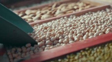 Metalik kepçe dar bir tepsiden kuru fındık alır ve onları büyük bir metalik kepçe iç kuru fındık kürekle ve onları geri bir dar ahşap Pan bir pazarda açık havada bırakma Arty makro çekim aşağı düşer