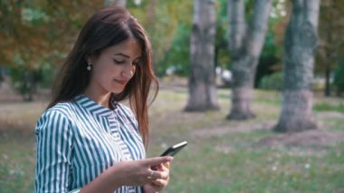 Gülümseyen ve yeşil park profil bir büyüleyici genç brunet içinde kadın ayakta, romantik gülümseyen ve sümer yeşil bir arka sokakta net sörf bir çizgili, net sörf uzun bağsız kıl ile neşeli kız