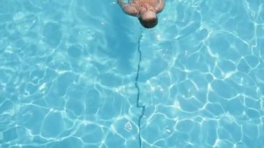 Gülümseyen, rahat sarışın kadın slo-mo Inspiring mavi bikini rahatlatıcı bir gülümseyen görünümü sarışın kadın ve bir yüzme havuzunda yüzme sırtüstü ağır çekimde turkuaz suları ile aşağı yukarı bir kürek çekmeye havuzda Sırtüstü yüzme