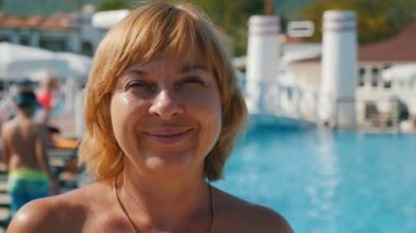 Sarışın kadın ayakta ve ayakta ve gülümseyen güneşli bir yavaş hareket turkuaz suları parlayan ile deniz kıyısında altın bir zincir ile neşeli sarışın bir kadın portresi slo-mo, yaz aylarında deniz kıyısında gülümseyen istirahat