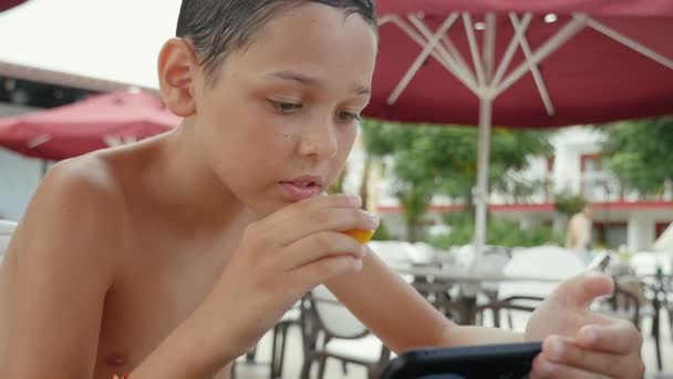 Μικρό Αγόρι Τρώει Και Σερφάρετε Στο Διαδίκτυο Ένα Καφέ Ένα — Αρχείο Βίντεο