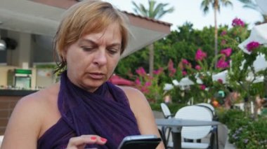 Oturma ve telefon net açık havada yaz bir kafe açık havada oturma ve smartphone kaydırma net sörf zarif bir elbiseli çekici bir sarışın kadın özgün görünümüne tarama glamour sarışın kadın çekimde fotoğraf