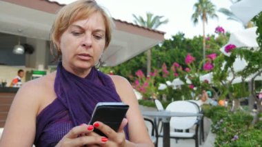 Oturan güzel sarışın kadın ve sörf net telefon açık havada yaz etkileyici görünümü içinde bir şık bir seksi sarışın kadın elbise bir kafe açık havada oturma ve emais çekimde gönderme smartphone net tarama