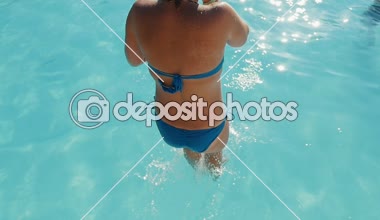 Sarışın kadın ayak ilk transparan bir yüzme havuzu atlama heyecanlı görünümü ayak ilk duru suları ile wading bir havuzda slo-mo güneşli bir atlama bir mavi swimmingsuit içinde neşeli bir sarışın kadın sular 