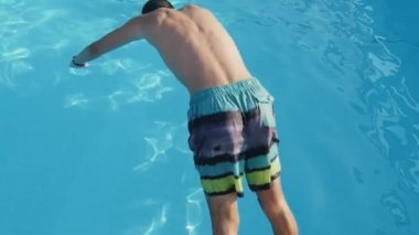 Ayak ilk baş sportif genç esmer adam dalış bir yüzme havuzunda ilk duru ışık mavi suları ile slo-mo komik görünümünde bir yüzme havuzunda yaz slo-mo atlama uzun şortlu genç adam
