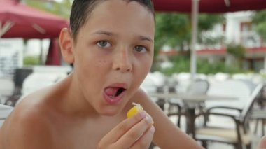Küçük çocuk bir ekşi limon bir deniz resort kafeteryada güneşli bir yaz neşeli görünümünde küçük bir brunet çocuğun gülümseyen ve güneşli bir yaz aylarında bazı deniz resort açık bir kafeteryada taklit eden sarı limon yemek yeme.