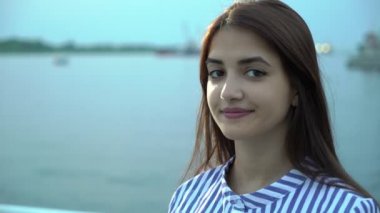 Mutlu yaz saçını sırayla yaz aylarında nehir iskele üzerinde koyarak zarif bir çizgili elbise şık uzun bağsız kıl ile gülümseyen bir brunet kadın harika manzarasını Dnipro Nehri'nin suları gülümseyen neşeli genç kadın