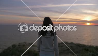 Muhteşem günbatımı yavaş, yavaş hareket bir ışık kazak daimi bir ince genç esmer kız arka görünümü bir deniz kıyısında yaz aylarında gün batımında bir sahil üzerinde duran romantik genç kadın