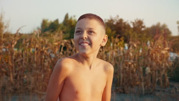 小男孩在湖岸上的水流下笑着 看到一个10岁的男孩在湖岸上的水下笑着 他拿着拐杖 在一个阳光明媚的日子里 在懒散的一天里 他被芦苇芦苇 — 图库视频影像