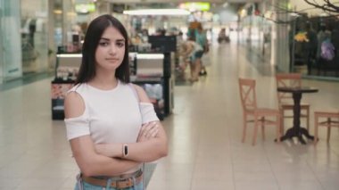 Neşeli genç esmer kadının ellerini ve gülümseyerek mutlu bir bluz ve onun ellerini haçlar tutmak ve sevinçle gülümseyen insanlarla dolu bir modern çarşıda kot cheerul ince genç kadın portresi bir alışveriş merkezinde haçlar