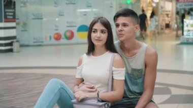 Mutlu genç çift bir kenara seyir ve bir alışveriş merkezinde yaz duygusal romantik bir genç kız görünümünü çatırdamak ile konuşma ve havadar bir alışveriş merkezinde şık brunet sevgilisi ile tüketici ile oturan uzun bağsız kıl