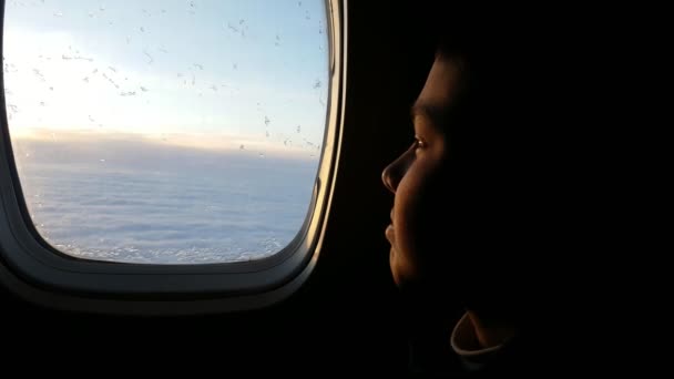 航空機窓の外を見て 飛行機の窓に座っていると考え 居心地の良いサロンで彼の人生を夢見てそれを探して Sportsuit で黒髪少年のエキサイティングなビューのサロンで夢の小さな男の子 — ストック動画