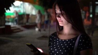 Romantik genç kadın gece yaz Bokeh görünümünde onu Smartphone cep telefonu ile aydınlatılmış City yaz geceleri sokak net sörf şık benekli elbiseli güzel bir esmer kızın telefonunu bir şehirde net tarama