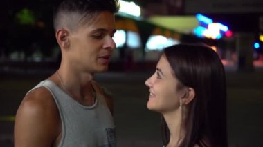 Şanslı chap ve gülümseyen sevgilisi City yaz heyecanlı görünümünde bir gri bir-gömlek ve güzel bir kız mutlu bir brunet adamın geceleri sokak konuşuyor ve yaz aylarında bir sokakta gülümseyen uzun bağsız kıl sohbet