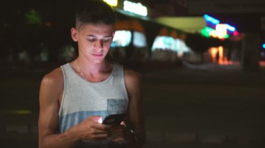 Akıllı genç adam telefonunu bir şehirde sokak gömlekli bir gri bir-onun smartphone bir şehirde yaz geceleri sokak üzerinde net sörf kısa saç kesimi ile yaz çabuk brunet adam portresi gece internette tarama
