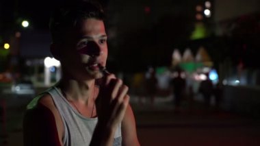 Vaping e-sigara bir şehirde sokak gece yaz Bokeh görünümünde elektronik sigara ve yaz geceleri duman şehir içinde ağız yoluyla dışarı nefes kolsuz tişört yakışıklı bir genç adam çabuk brunet adamdır