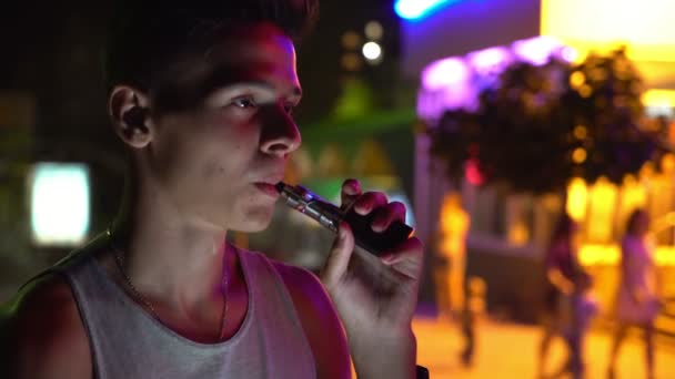 Молодой Человек Улыбается Курит Электронную Сигарету Городской Улице Ночью Летом — стоковое видео