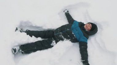 Karda yalan ve beyaz karda yalan ve elleri ve ayakları Tatras komik bir şekilde sallayarak sportif kış elbiseli bir on-yıl-yaşlı çocuk onun ellerde ve mutlu bir şekilde iyimser görüş hareketli bir kayakçı'nın elbiseli küçük çocuk