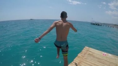 Çalışan ve ayakları açık denizde slo-mo uzun şort ayak ilk mavi deniz sularında yavaş yaz aylarında güneşli bir atlama sportif bir genç adam neşeli görünümünü Türkiye'de ilk atlama brunet delikanlı