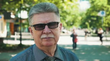 Mutlu emekli adam ayakta ve kendinden emin bir komuta sizde slo-mo neşeli görünümünde bir sokakta gülümseyen bir sokakta duran ve iyimser slo-mo yaz aylarında güneşli bir sokakta gülümseyen beyaz bıyıklı siyah güneş gözlüğü