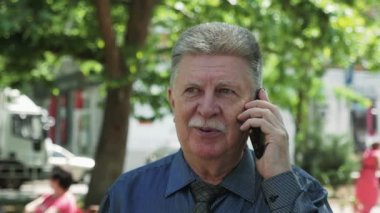 Yaşlı adam onun telefon slo-mo bir gülümseyen neşeli görünümü bir sokakta duran üst düzey konuşurken jolly adam şaka ve onun smartphone bir yeşil sokak ağır çekimde yaz aylarında konuşurken su kuyusu-damat bıyıklı