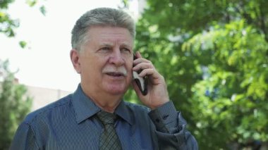 Kendine güvenen komuta sizde onun smartphone yavaş yaz aylarında yeşil bir parkta dururken konuşurken düzgün bıyıklı yavaş hareket saygın bir beyaz saçlı adam harika manzarasını yeşil bir parkta yaptığı telefon sohbet