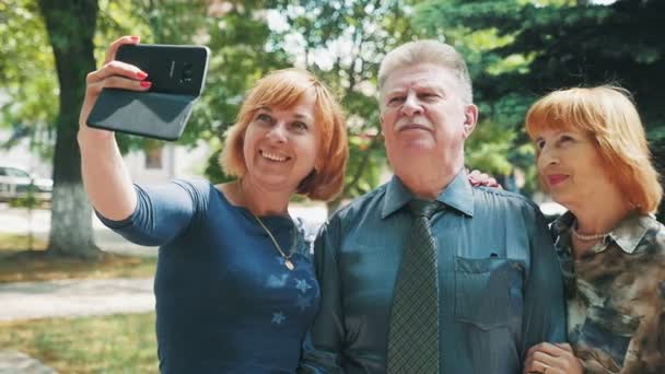 幸せな金髪女はスローモーションで夏に公園で白髪両親と一緒に Selfie を取ってボブのヘアカットとスローモーション笑顔金髪女性の陽気な視点でシニア両親と共に Selfie を取っています — ストック動画