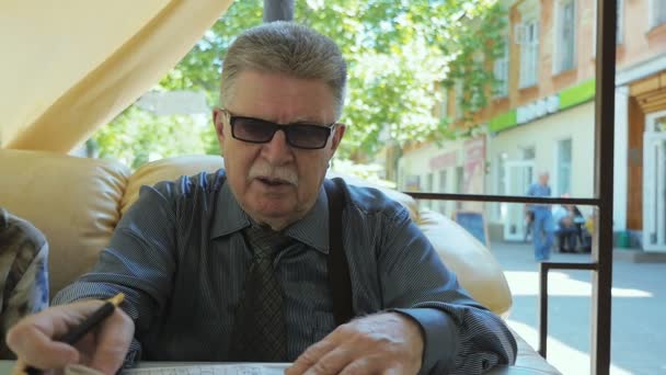 Ανώτερος Άνθρωπος Κάθεται Και Λύνοντας Σταυρόλεξα Μια Καφετέρια Καλοκαίρι Αργή — Αρχείο Βίντεο