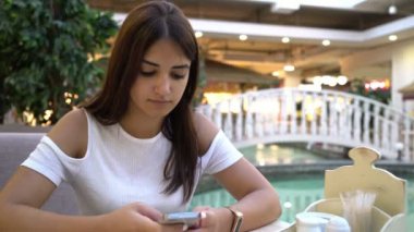 Güzel kız mesaj sms onun smartpnone mavi çeşmeden onun akıllı bir kafeteryada bir zarif bluz manifatura bir ileti içinde neşeli genç esmer kadın şaşırtıcı görünümü, bir kafede üzerinde güzel bir gölet yakınındaki