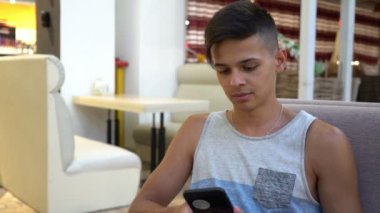 Oturma ve rahat bir kafeterya onun smartphone hakkında bilgi kaydırma çizgili bir tank top kısa saçlı modern Café etkileyici bir sportif esmer adam görünümünü telefonuna net sörf şık genç adam