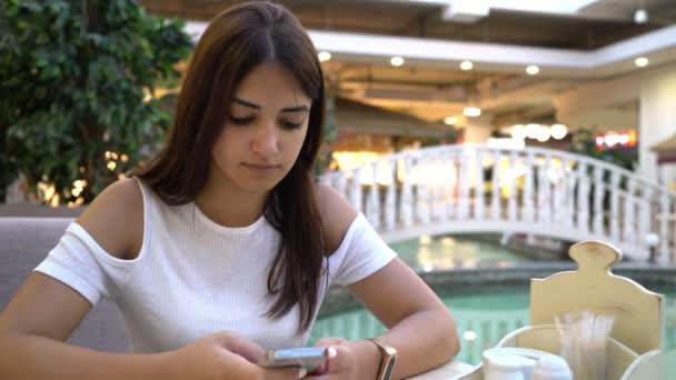 Superbe fille textos sms sur son smartpnone dans un café à une fontaine bleue Vue étonnante de jeune femme brune gaie dans un chemisier élégant textos un message sur son smartphone dans une cafétéria près d'un bel étang 