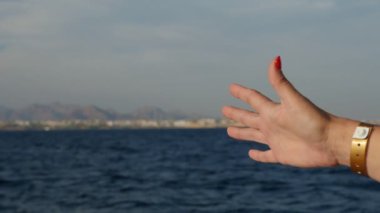 Deniz rüzgar yavaş hareket şaşırtıcı görünümünde bir el ile Mısır'daki bir gemiden dokunmaya çalışan kadının palm ağır çekimde güneşli bir günde, Sharm El Sheikh parmak, kırmızı manikür ve bir kol saati bir gemide açma