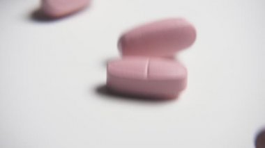 Vitamini pastilleri, haddeleme dans ve yavaş hareket neşeli makro beyaz bir tablo üzerinde oyun oynama ve beyaz studio tablo çekimde döne döne pembe tablet vurdu. İyimserlik ruhu şekil.