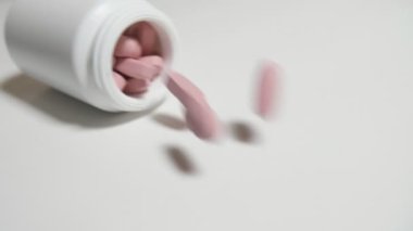 Pembe pastilleri yavaş yavaş çekimde bir beyaz studio tablo üzerinde açık bir kap ile beyaz bir plastik paket dışarı atlama pembe hap etkileyici makro çekim bir tablo üzerinde beyaz bir plastik tüp dışında atlama
