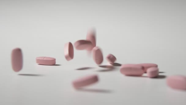 Des pastilles roses sautent et tournent sur une table blanche au ralenti Gros plan joyeux de pilules roses sautant et se déplaçant sur une table de studio blanche au ralenti. Ils génèrent l'esprit de santé .