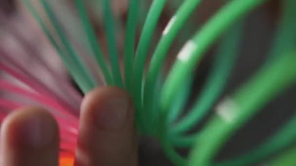 Doigts enfantins jouant avec un arc-en-ciel en plastique coloré slinky au ralenti Impressionnant macro shot d'un arc-en-ciel en plastique multicolore slinky avec des bobines mobiles maintenues par des doigts enfantins au ralenti. Ça a l'air drôle .