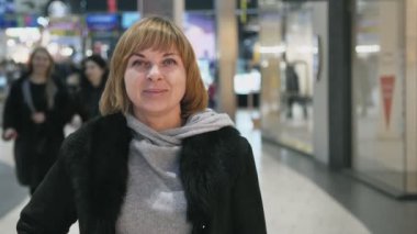 Bir alışveriş merkezi ile havadar bir gülümseyen ağır çekim iyimser portresi koridorlarda sarışın kadın siyah ceket şık bir saç kesimi ve sportif bir kazak bir alışveriş merkezinde slo-mo ile gülümseyen güzel kadın
