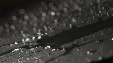 Yağmurlu su damla, ağır çekim rüya gibi makro sıçramasına arasında uzanan ince kitapçık arasında yağmurlu boncuk slo-mo engebeli bir siyah yüzey üzerinde hareket ince akışların vurdu. Hayal bir ruh şekiller.